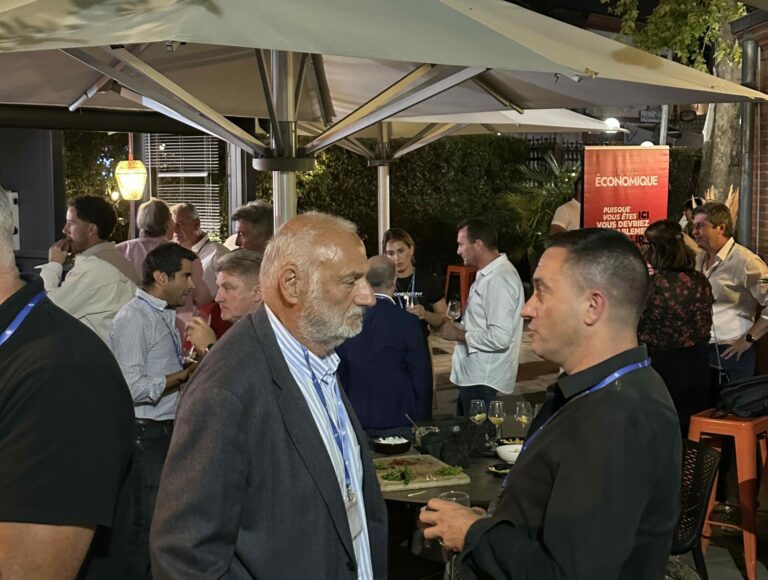 Des participants échangent debout autour de l’apéritif sur la terrasse de La Pergola, avec une bannière La Vie Économique en arrière-plan.